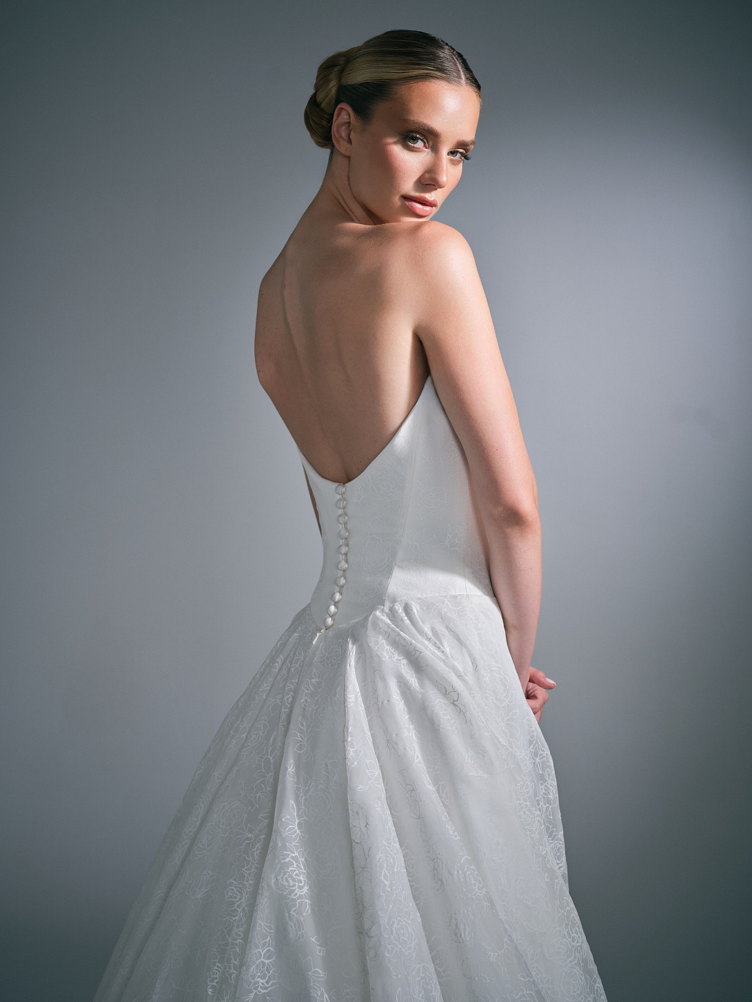 Side profile view of the Suzanne Neville Clovelle wedding gown, demonstrating the structured waistline and fabric drape