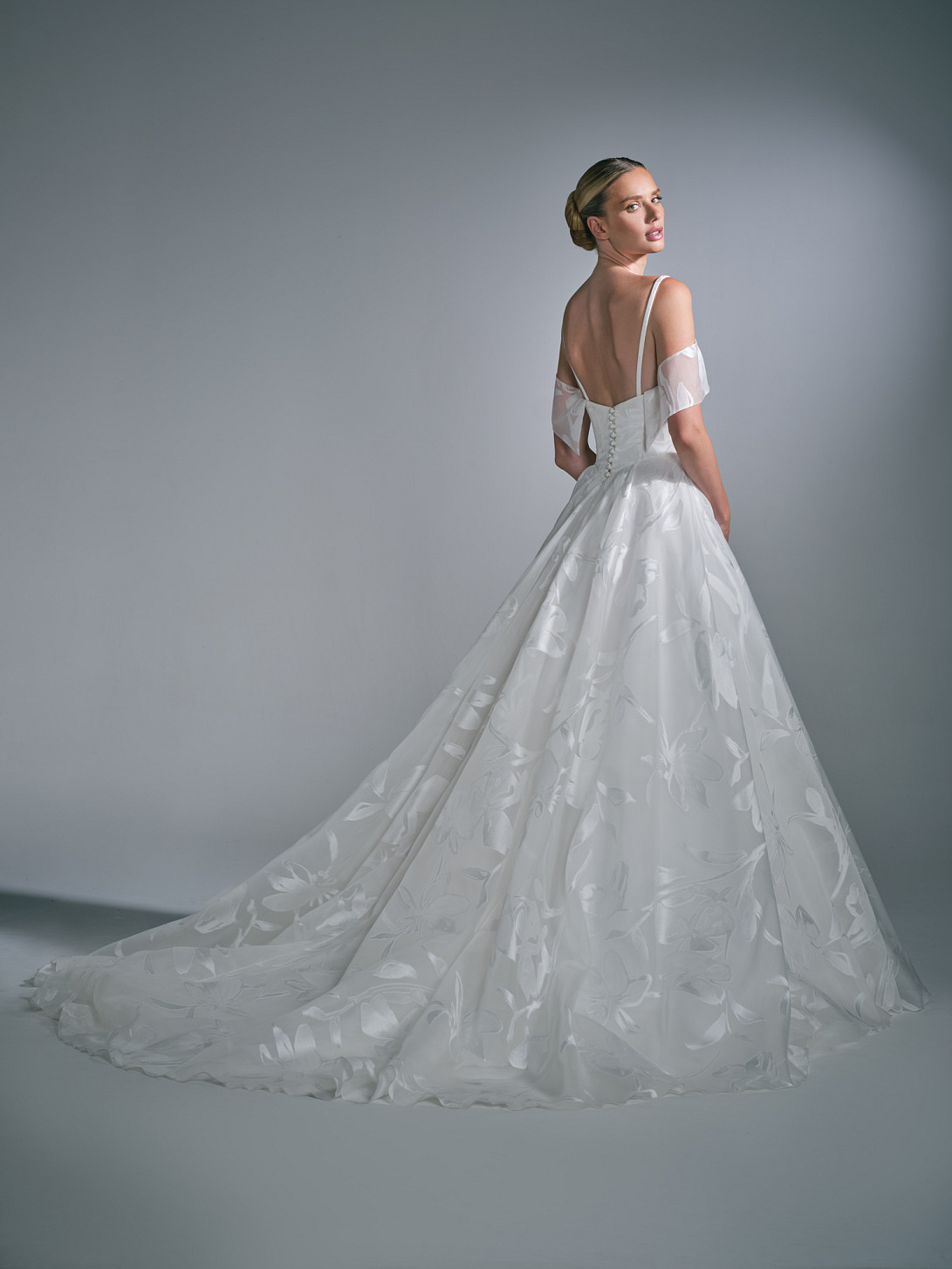Full-length back view of the Liora bridal dress, featuring classic fabric-covered buttons along the corset spine leading down into a sweeping train and detachable collar
