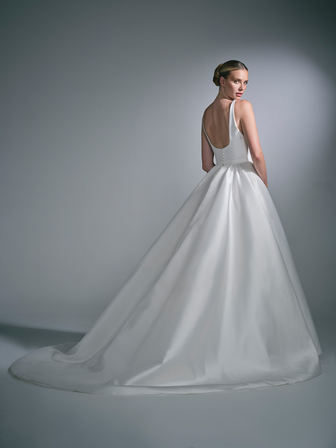 Back view of the Lysenne wedding dress by Suzanne Neville, featuring signature covered buttons down the spine and a sweeping skirt train.